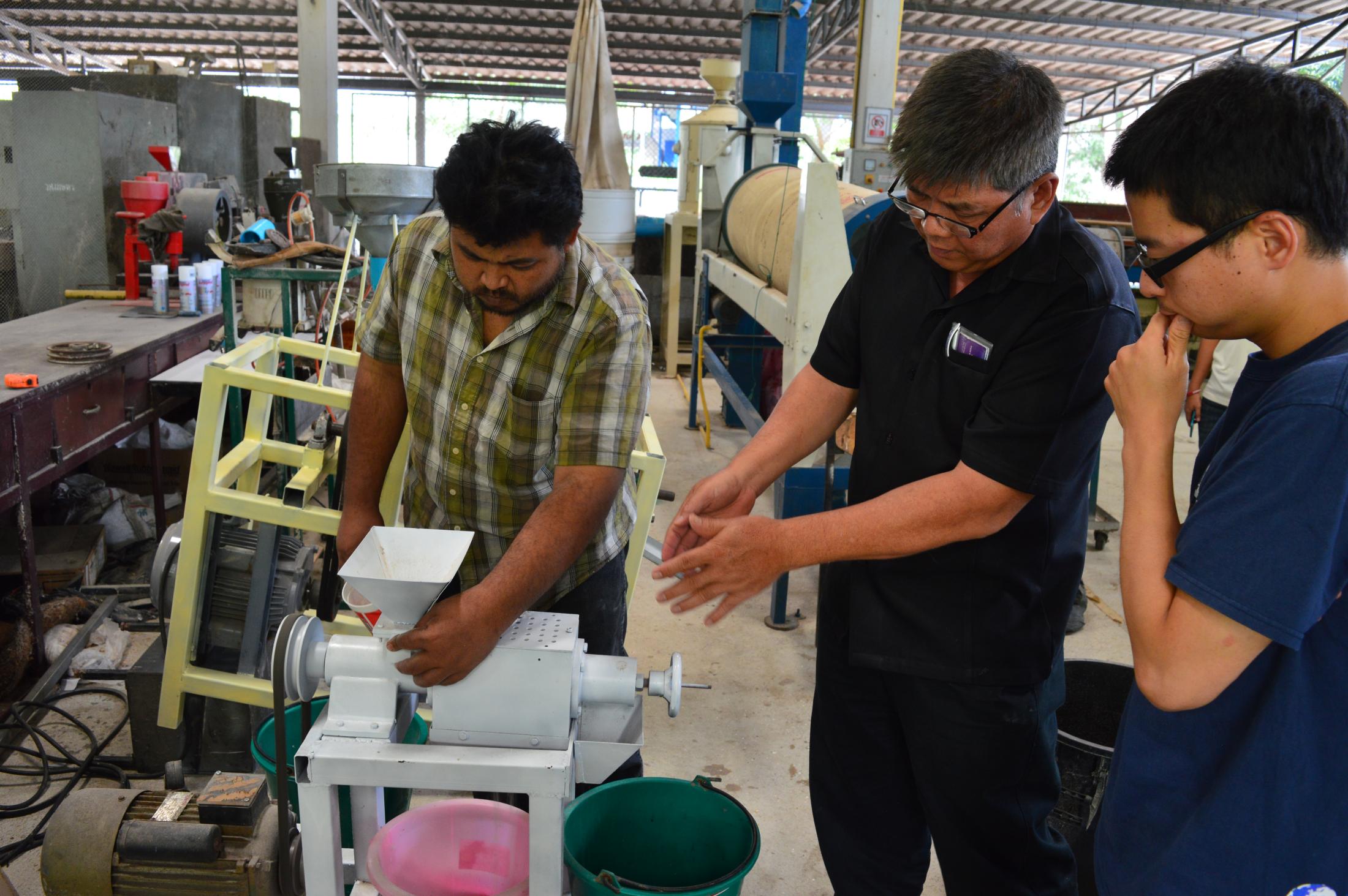 Professor, staff member and student gather around machine in a workshop setting.