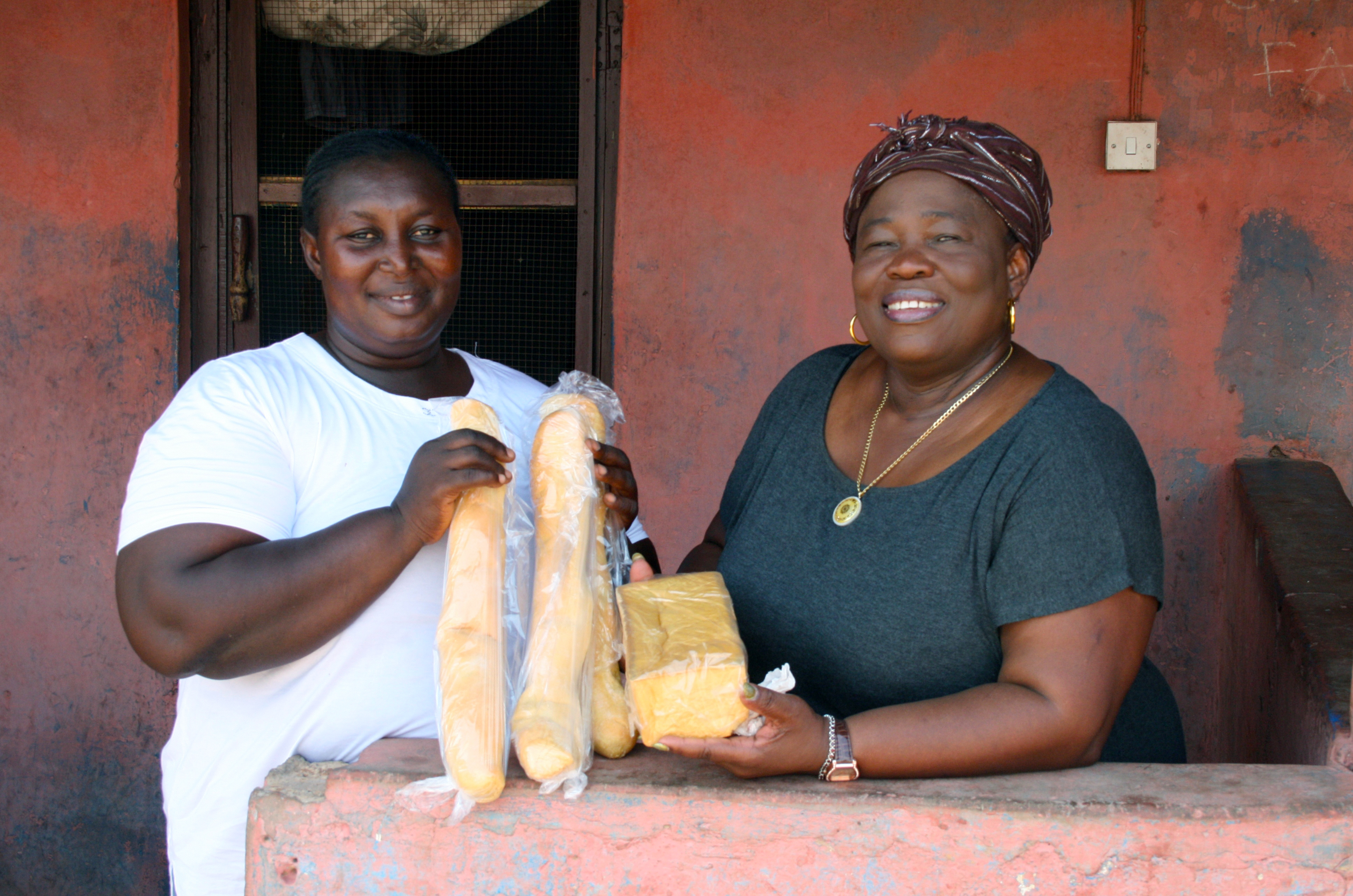 Two women hold various orange bread loafs and cakes.