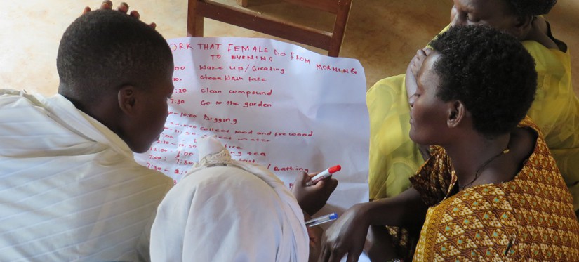 Four people gather around a large piece of paper they are writing on with red marker