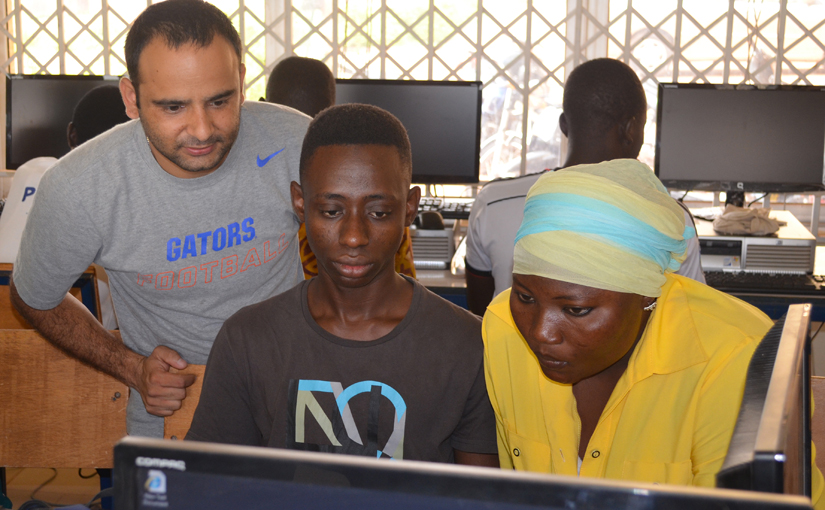 Paudel stands behind two students that work on computers