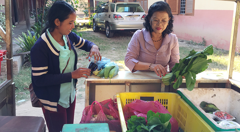 farmer selling fresh vegetables to a woman from bins in a trailer