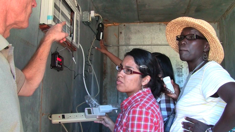 three women looking at man's arm pointing to air conditioner and CoolBot controller