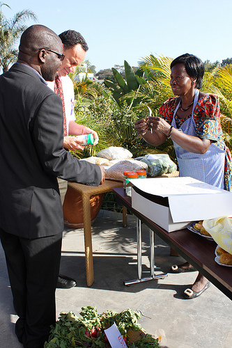 Woman standing behind table with apron shows something to two men