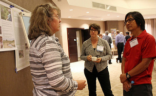 Three people standing talking in a room with posters on the wall behind them