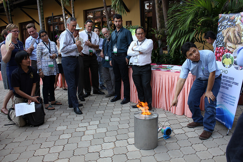 Group looks on as Thansrithong points to a stove with an open flame