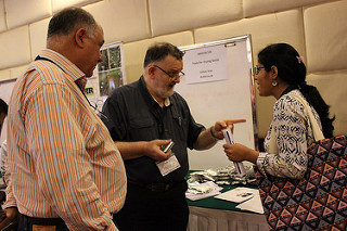 Van Asbrouck and Mukherjee discuss in front of tables with a posters, Alvarado-Downing looks on