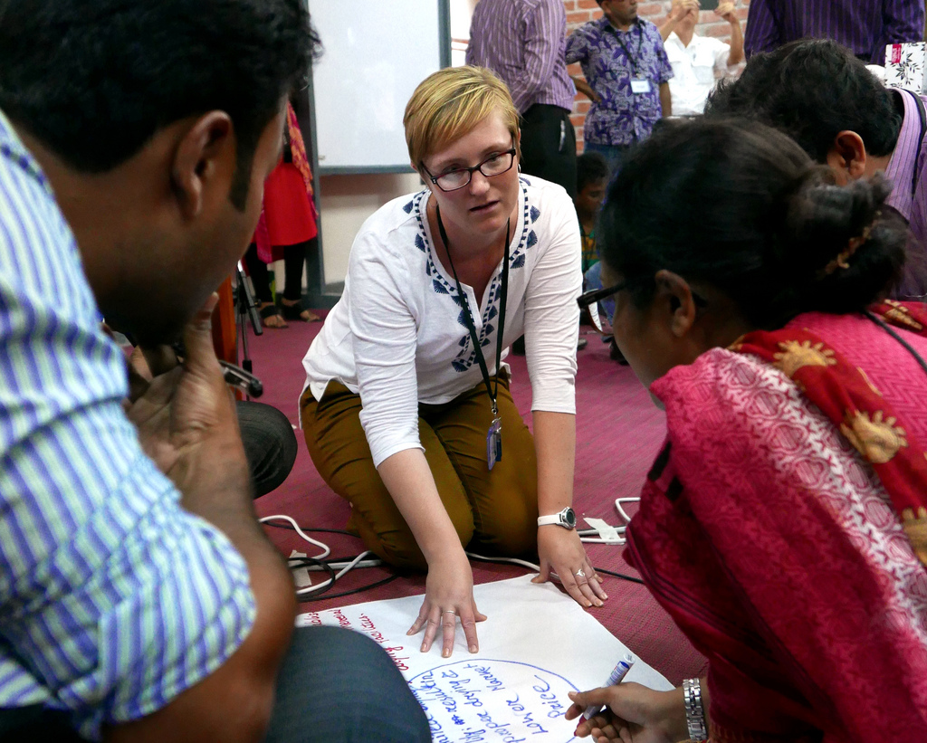 Hansen crouches on the ground speaking and gesturing to a poster, group of trainees around her