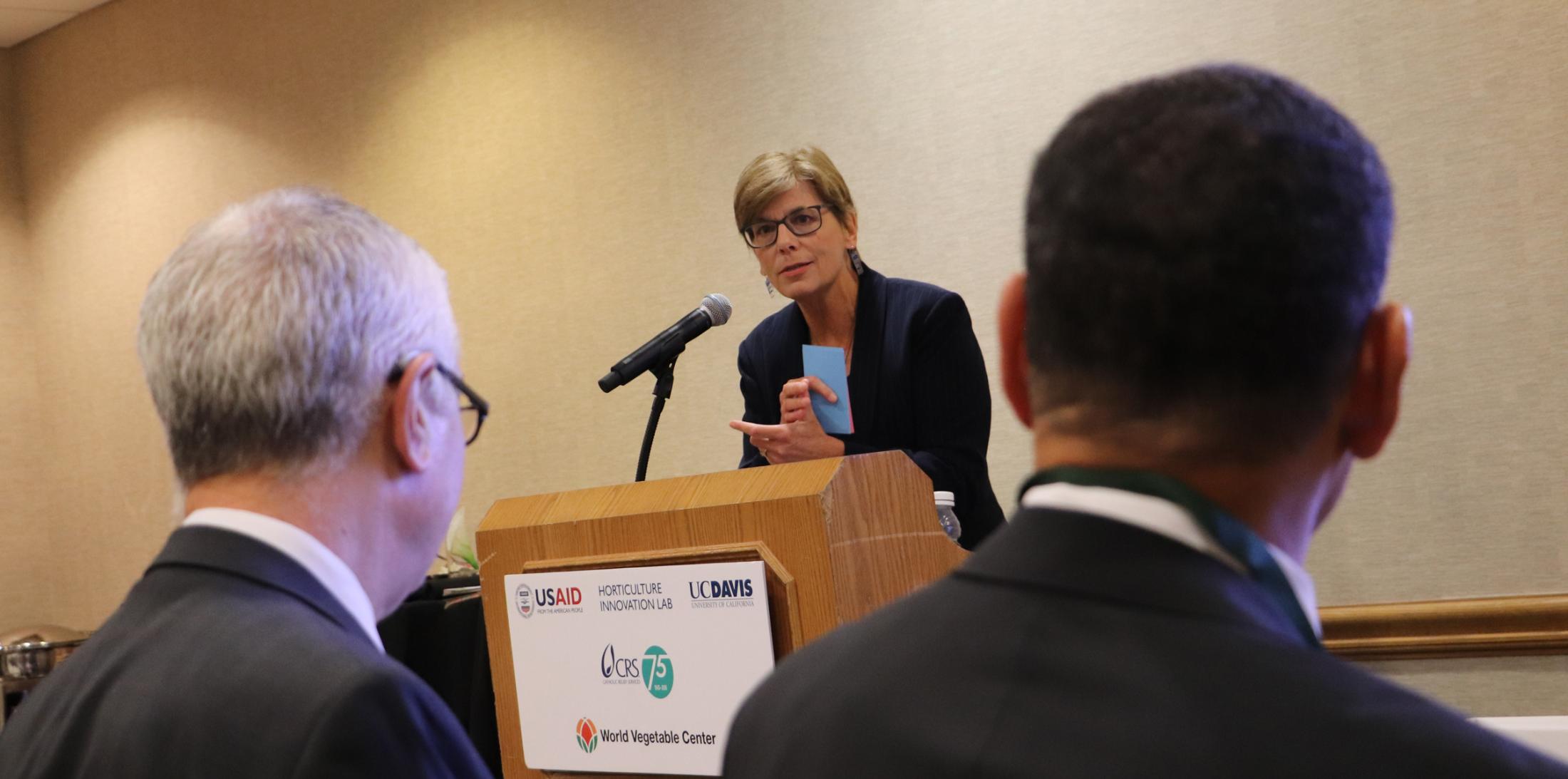 speaker at podium with Rob Bertram and John Bowman in the audience at World Food Prize 2018 side event