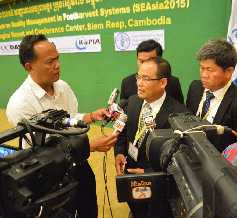 Man in suit surrounded by reporters with microphones and video cameras