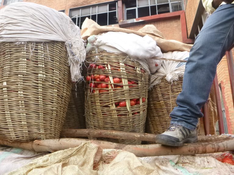 tomatoes peek out between cracks in bulging woven crates on a truck