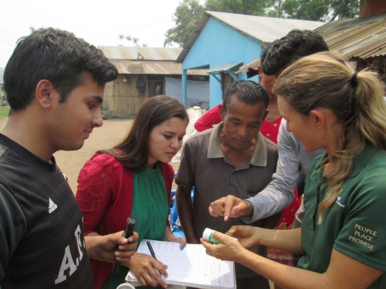 Young man pointing to pH strip indicator, with older man looking on, along with other students and Tiare holding the test strips