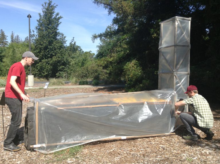 two men adjust plastic cover over chimney solar dryer outdoors