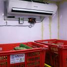 Photo of the coolbot hooked up to an air conditioner above produce crates