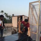 Two researchers connect a black table to a clear chimney to build a solar dryer