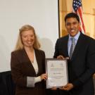 Elana accepts award plaque from USAID leader, American flag in background